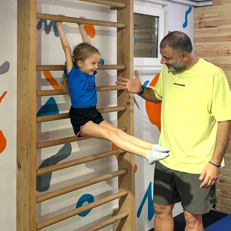 Man assisting a child on a wooden攀爬架 in an indoor play area.