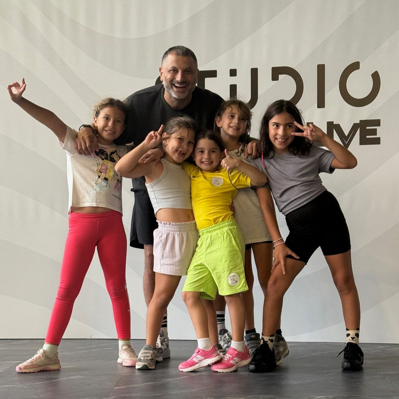 Group of children and a teacher posing in a dance studio with 'Studio Live' branding.
